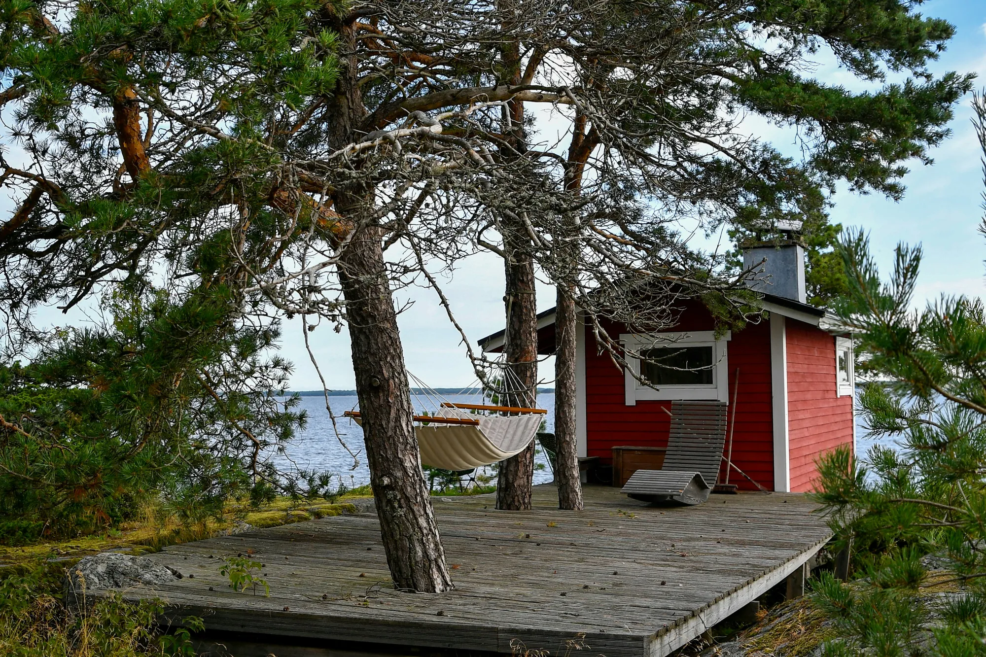 Punainen mökki mäntyjen katveessa järven rannalla Joensuun seudulla